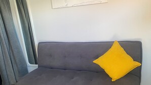 En grå sofa med træben og en gul pude.
