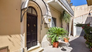 A narrow alleyway with a black door, potted plants, and a light fixture.