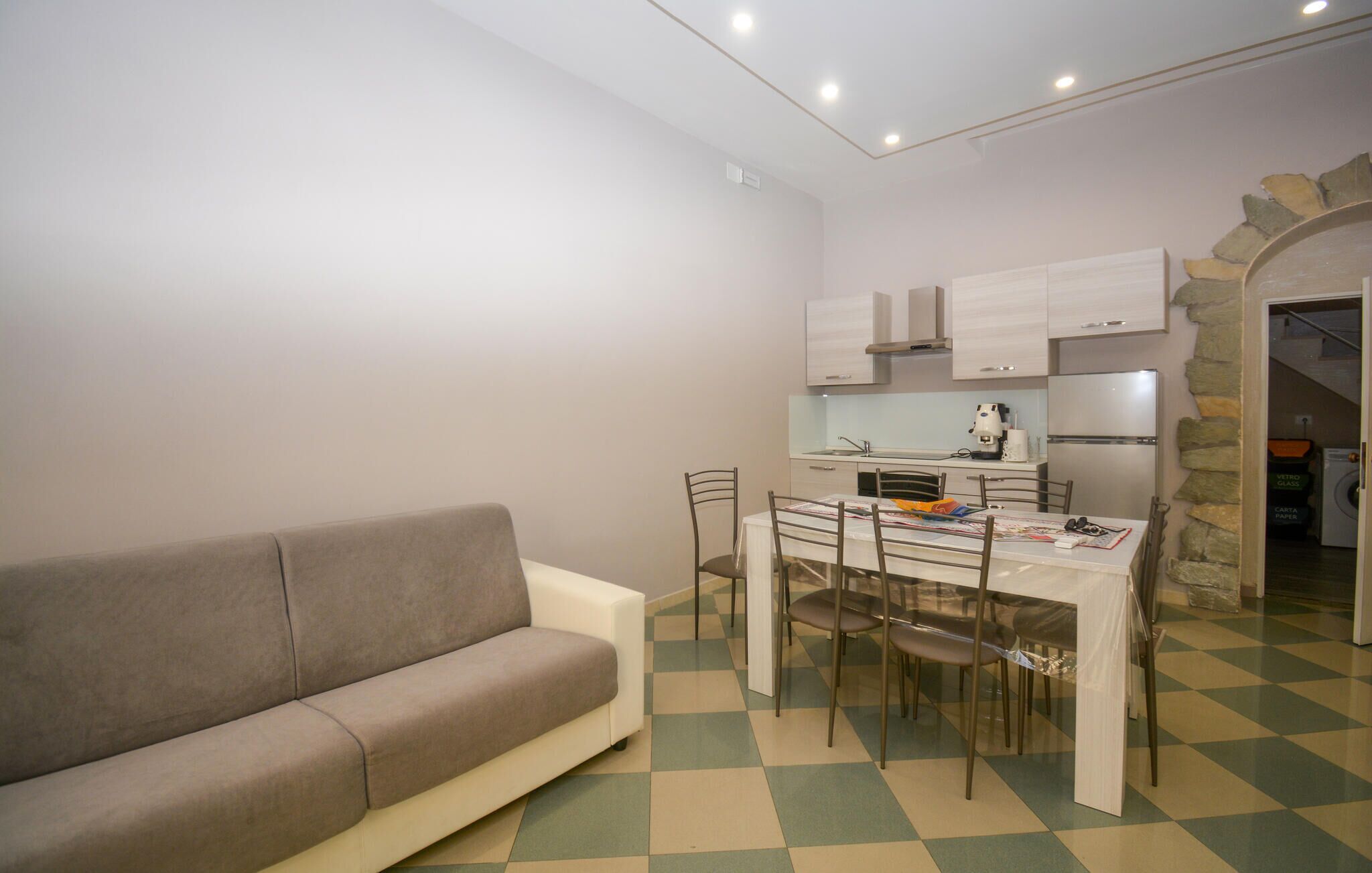 Een ruimtelijke woonruimte met een bank, eettafel, stoelen, een kitchenette en een zwart-wit betegelde vloer.