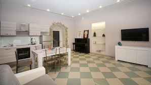 A modern kitchen with white cabinets, a dining area with a checkered floor, and a flat-screen TV mounted on the wall. - Cozy home in Solarino with WiFi (Solarino)
