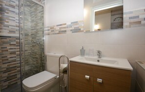 Un bagno con box doccia in vetro, un water, un lavandino con uno specchio sopra e un mobiletto in legno.