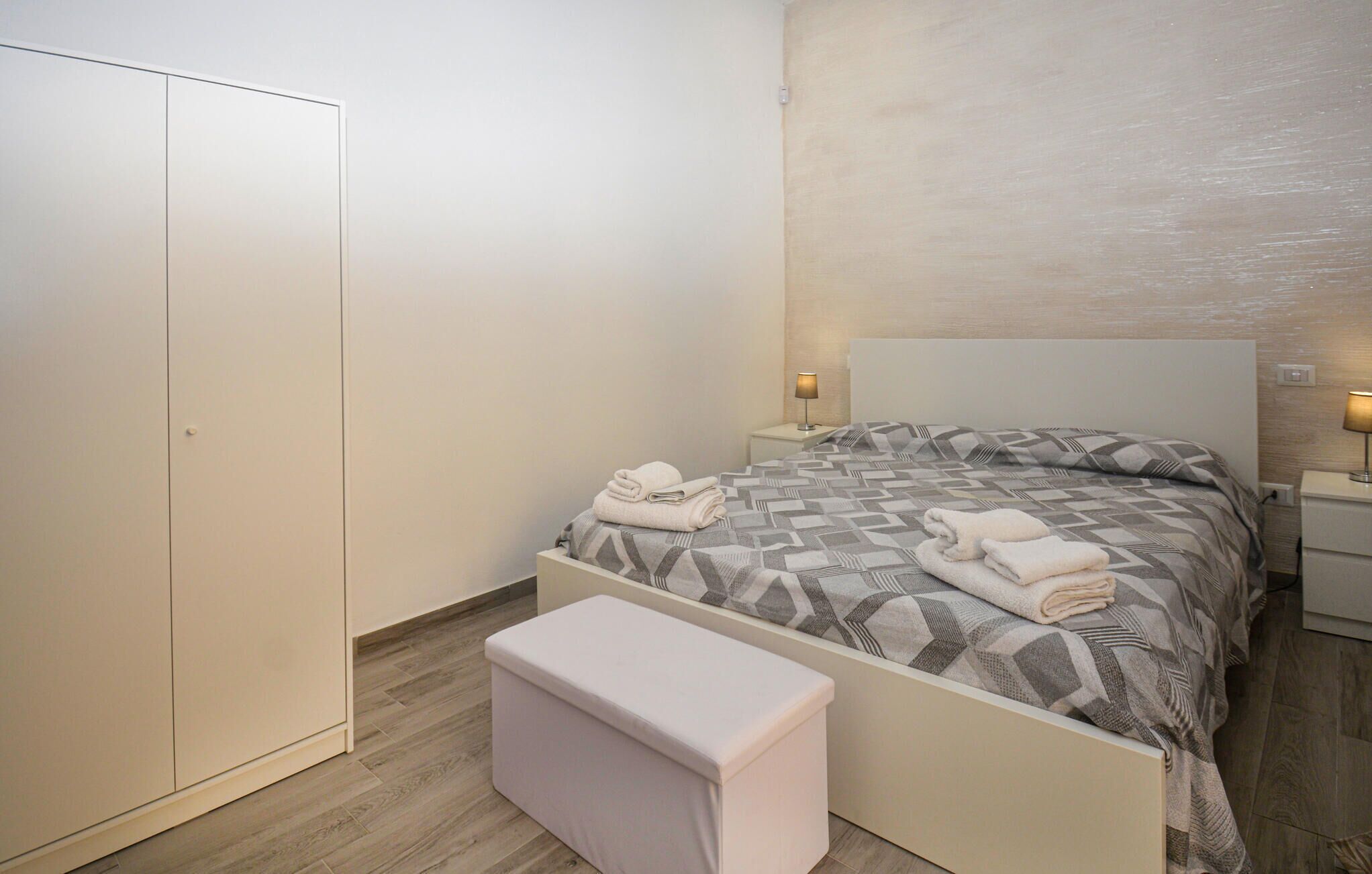 A bedroom with a bed, two bedside lamps, a nightstand, a wardrobe, and a bench.