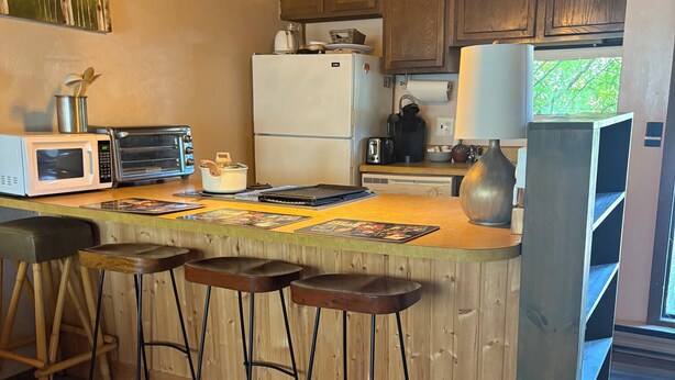 A kitchen with wooden cabinets, a refrigerator, a microwave, a toaster, and hanging pendant lights.