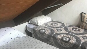 A small, single-bed room with a sloped ceiling, a patterned bedspread, and a pillow with a polka dot design.