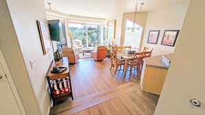 A spacious living area with a dining table, chairs, and a sofa. There is a large window providing a view of the outdoors. - River Village 331A 1 Bd, 1 Ba First Floor Condo (Bend)