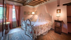 Een slaapkamer met een hemelbed, een nachtkastje met een lamp en een raam met gordijnen.
