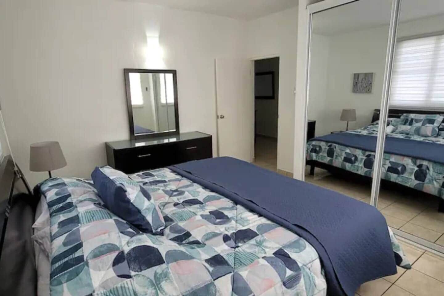 Une chambre à coucher comprenant un lit, une commode, un miroir et une porte donnant sur une autre pièce.