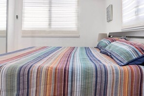 Un lit avec une couvre-lit à rayures, une tête de lit et une fenêtre avec des stores.