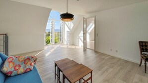 A spacious room with a high ceiling, a wooden table, a blue sofa, and a view through large windows to the outdoors. - 2 bedroom nice home in Harpelunde (Harpelunde)