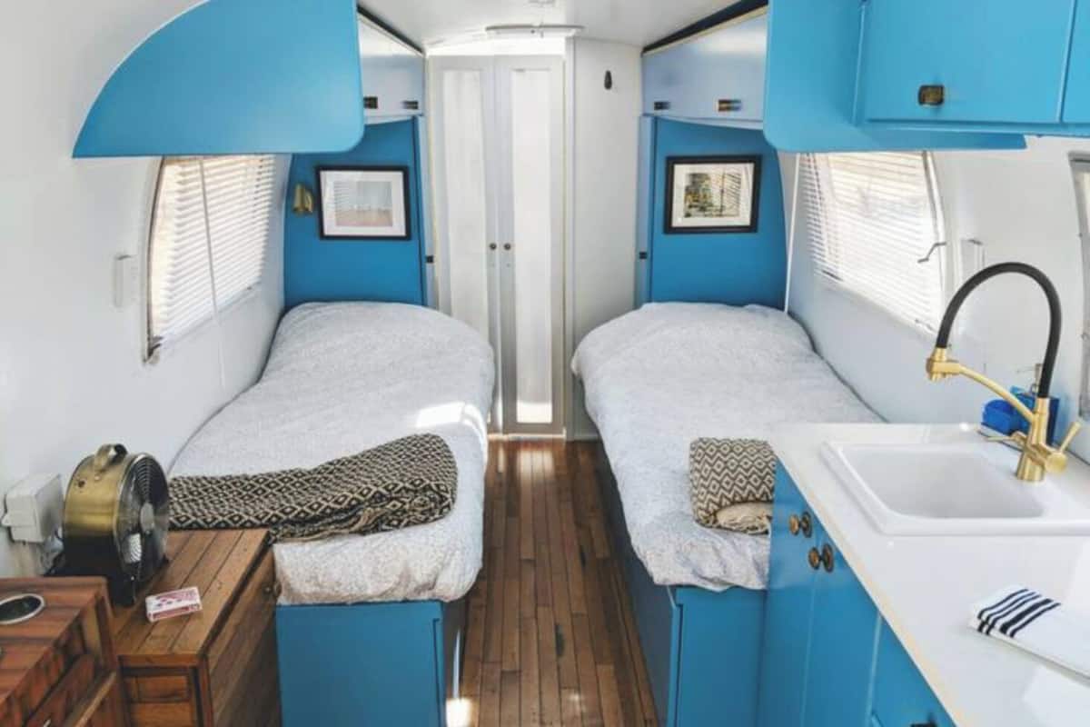 Un intérieur de camping-car compact comprenant deux lits, un évier et une petite table.