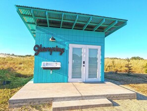A small, turquoise building with a sign reading "Glamping." It features a white door, a small sink, and a metal sign. - Vinyl Vineyards  (Paso Robles)