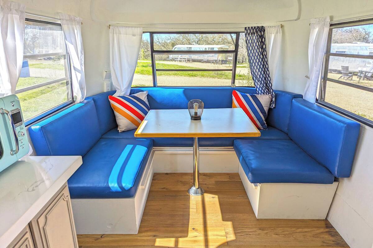 Un espace de vie compact comprenant un canapé bleu, une petite table et une fenêtre avec des rideaux.