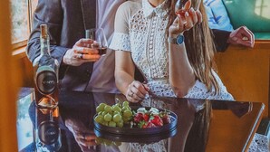 A couple seated at a table with a bottle of wine, a glass, and a bowl of grapes and strawberries. - Vinyl Vineyards  (Paso Robles)