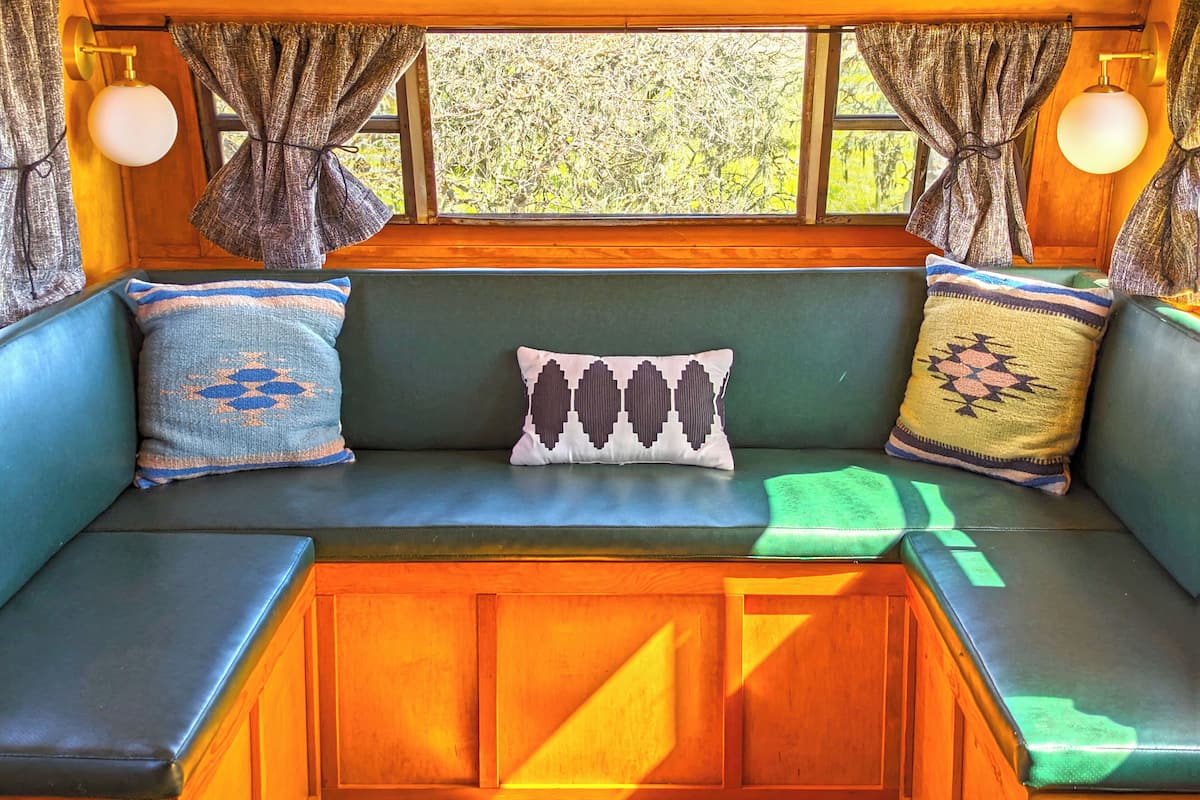 Un coin salon confortable avec un banc rembourré de couleur verte, des coussins à motifs et une vue sur la verdure environnante.
