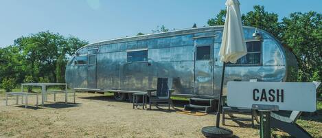 A vintage trailer with a "CASH" sign, outdoor seating, and a dining table.
