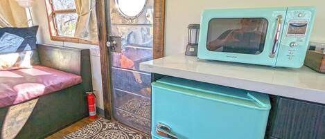 A compact kitchen with a vintage-style microwave, a small refrigerator, and a window with curtains.