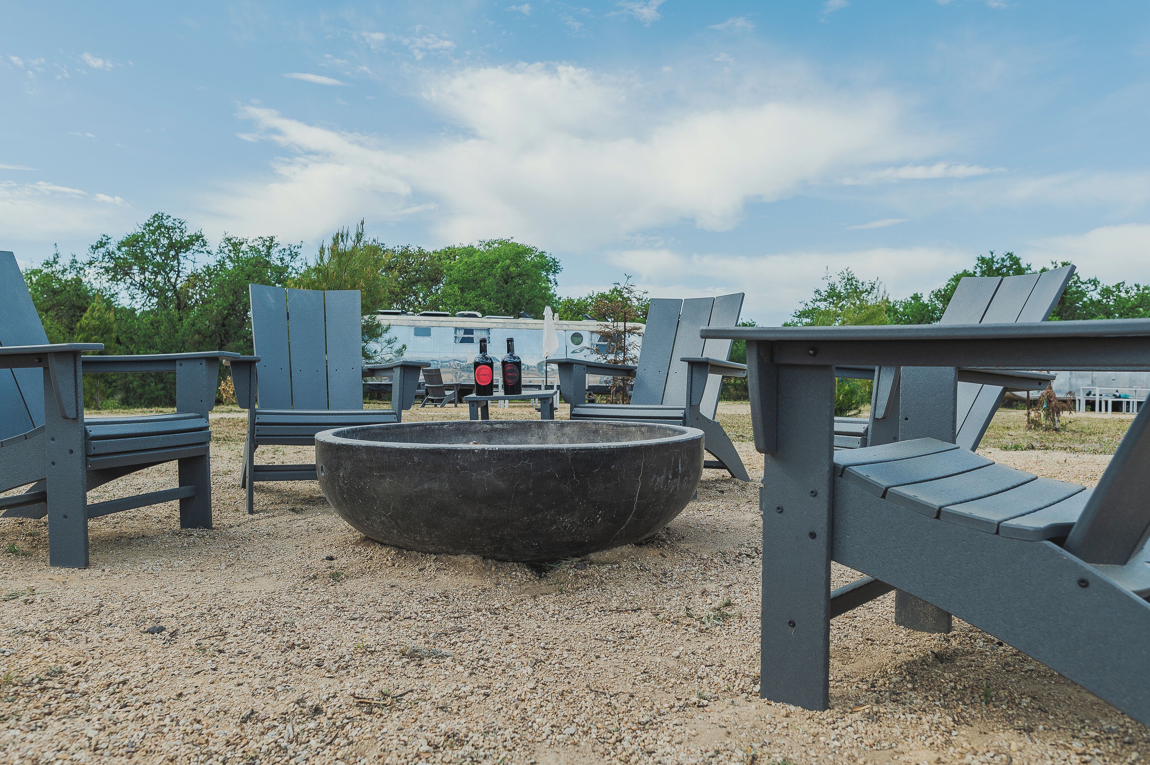 A gravel area with Adirondack chairs and a large fire pit.
