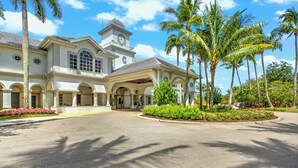 A large, two-story building with a central entrance, arched windows, and a clock tower. - Beautiful First-floor, End Unit, Coach Home in Fiddler's Creek, Naples, FL (Naples)