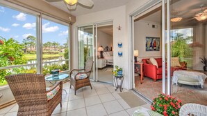 A spacious balcony with wicker furniture, a glass door leading to a living area, and a view of a lake and greenery. - Beautiful First-floor, End Unit, Coach Home in Fiddler's Creek, Naples, FL (Naples)