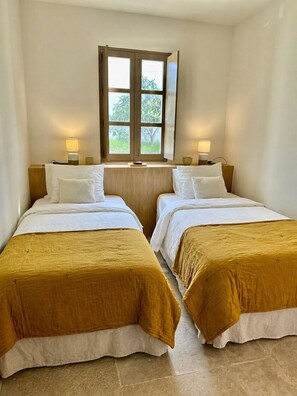 Une chambre avec deux lits, une fenêtre donnant sur un espace verdoyant et des lampes de chevet.