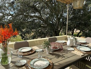 Une table dressée à l’extérieur, avec des assiettes, des verres et un vase rempli de fleurs.
