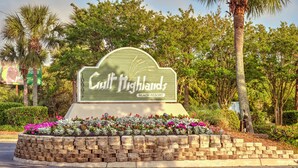 Schild für das Gulf Highlands Beach Resort, umgeben von einem angelegten Garten mit verschiedenen Pflanzen und Blumen.