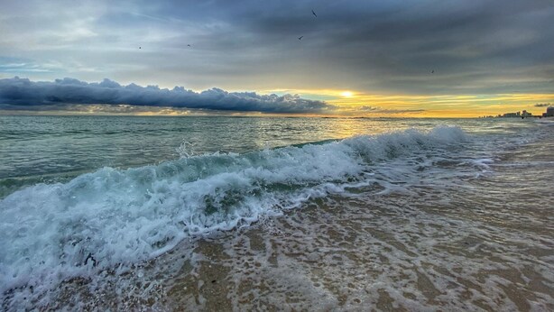 Ein Strand mit brechenden Wellen unter einem bewölkten Himmel.