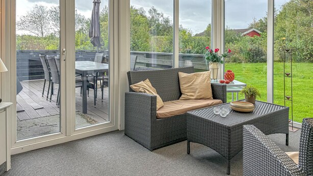 A sunlit patio area with a wicker sofa, a small table, and a glass door leading to an outdoor deck.