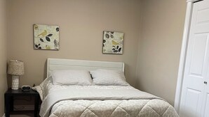 Une chambre à coucher comprenant un lit, une table de chevet, une lampe, deux œuvres d’art murales et une porte.