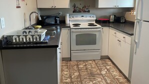 Une cuisine de taille réduite avec des meubles blancs, une cuisinière, un four à micro-ondes et un évier.