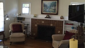A living room with a fireplace, two armchairs, a television, and a bookshelf. - Charming Santa Barbara Cottage (Santa Barbara)
