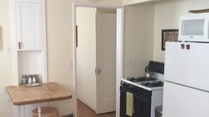A compact kitchen with a stove, oven, and microwave. There's a small wooden table with salt and pepper shakers. A bag is on the floor next to the table. - Charming Santa Barbara Cottage (Santa Barbara)