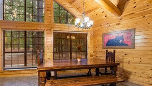 Une table à manger en bois avec des bancs, un lustre et un tableau représentant un ours accroché au mur.