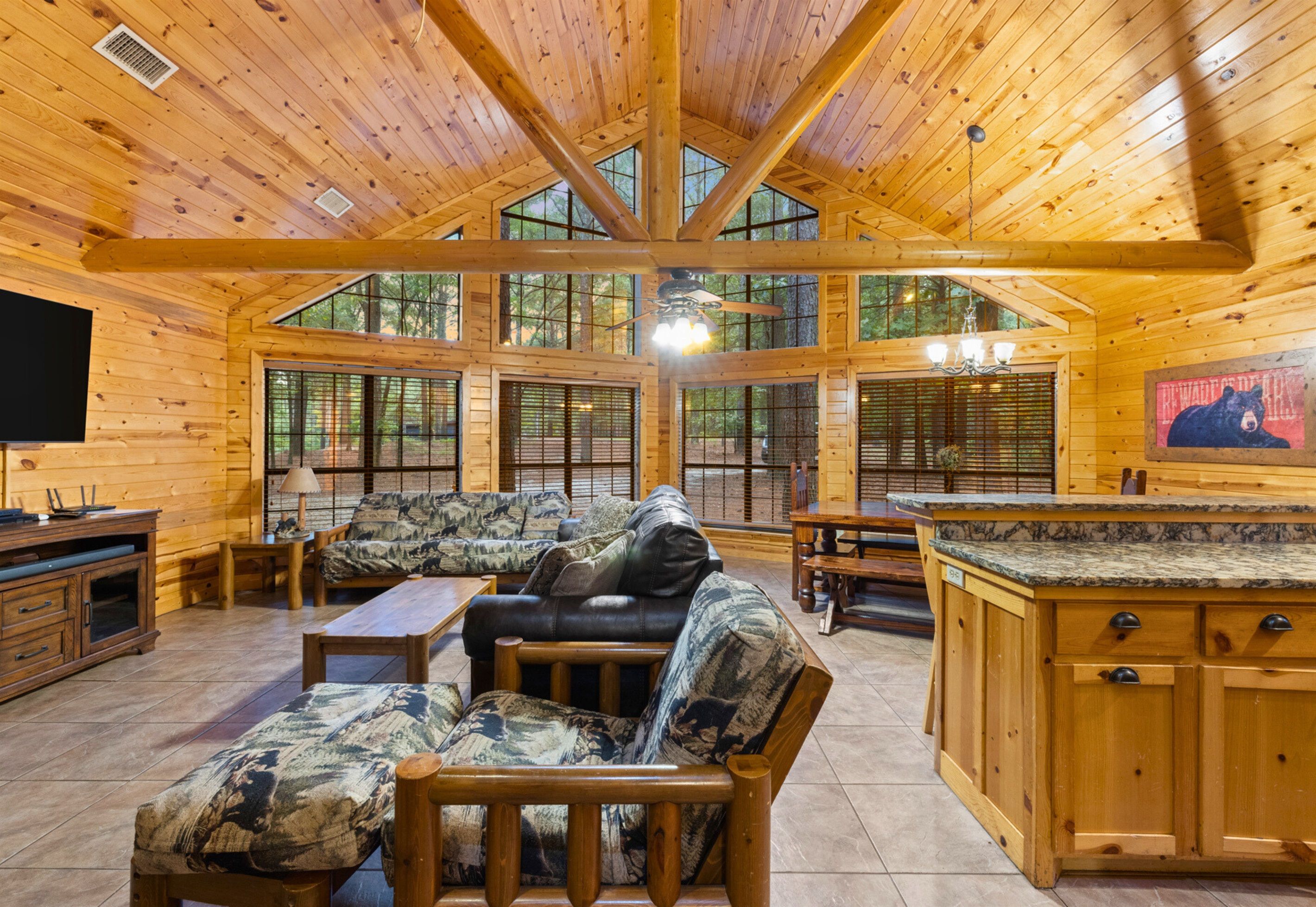 A spacious cabin interior with a high ceiling, large windows, a cozy seating area, and a kitchen with wooden cabinets.