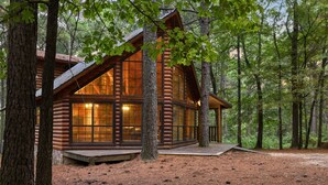 Une cabane en rondins dotée de grandes fenêtres, entourée d’arbres.
