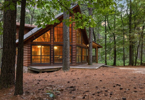 A log cabin with large windows, surrounded by trees.