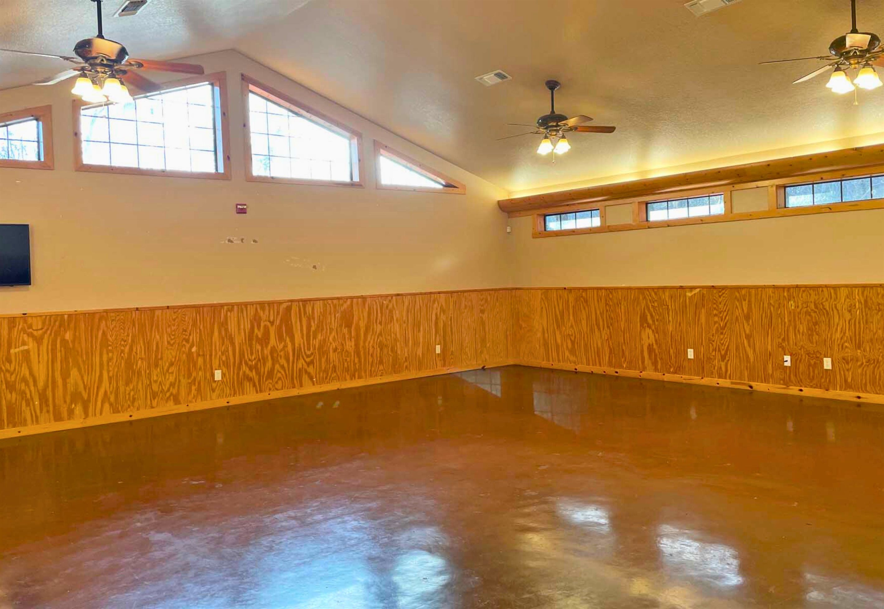 A spacious room with wooden paneling, large windows, and ceiling fans.