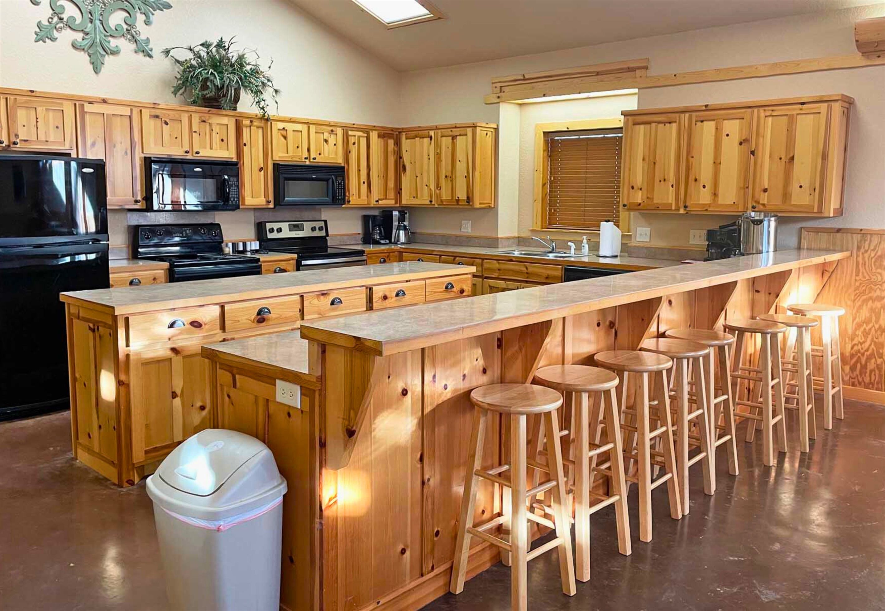 A kitchen with wooden cabinets, a central island with stools, and a trash bin.