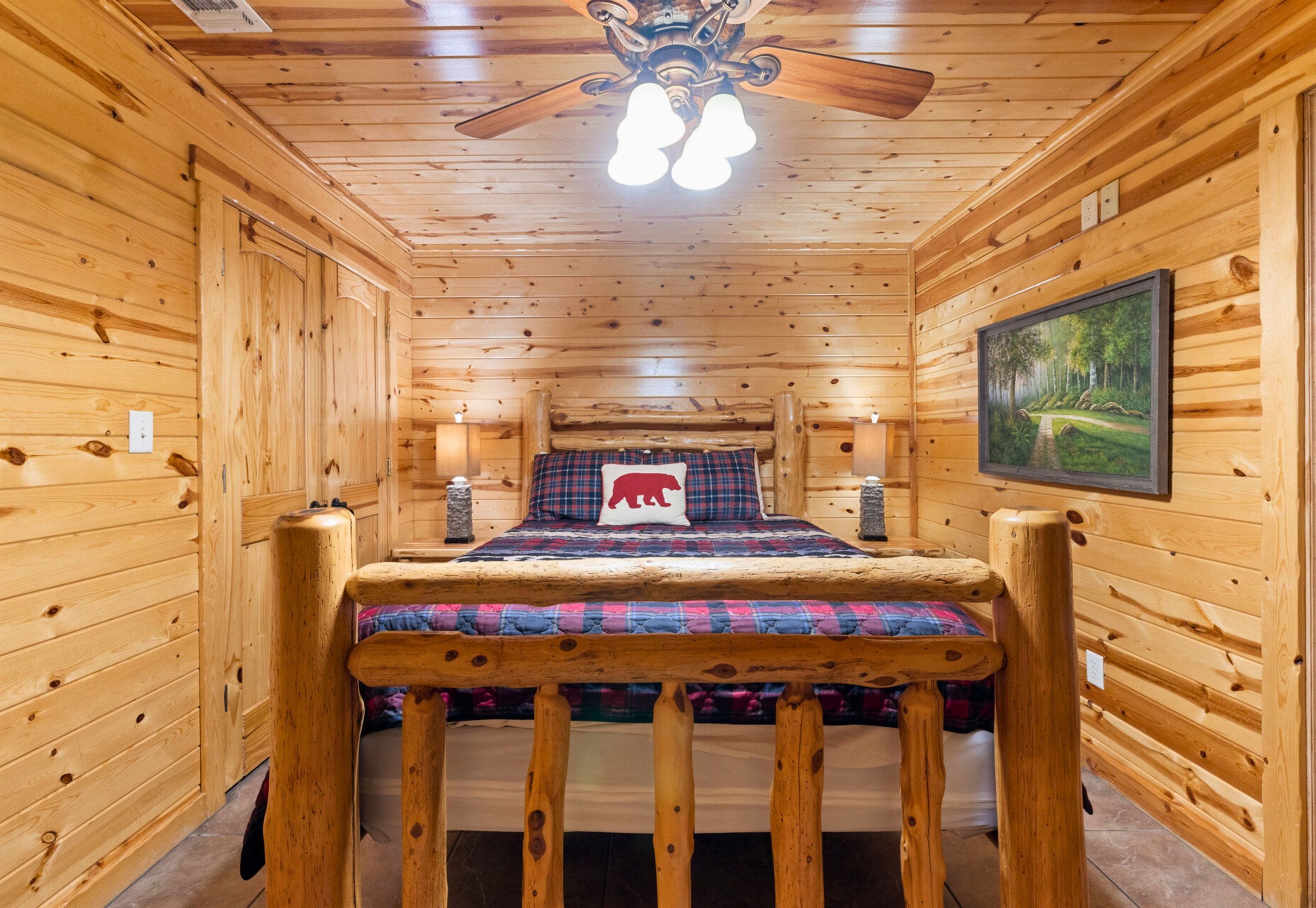 A wooden cabin room with a bed, a ceiling fan, and a painting on the wall.
