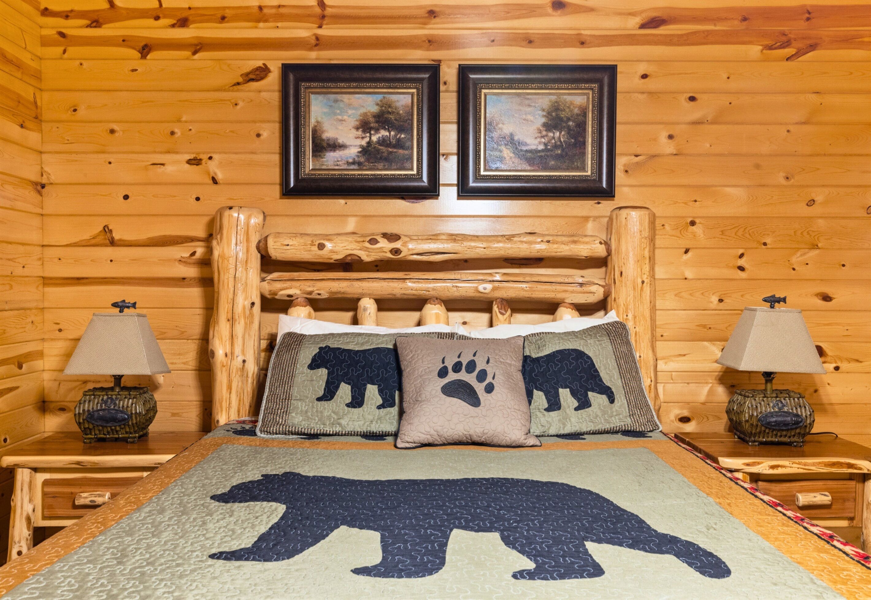 Een houten kamer met een bed, beddengoed met berenmotieven, twee landschapsschilderijen aan de muur en twee bedlampjes.