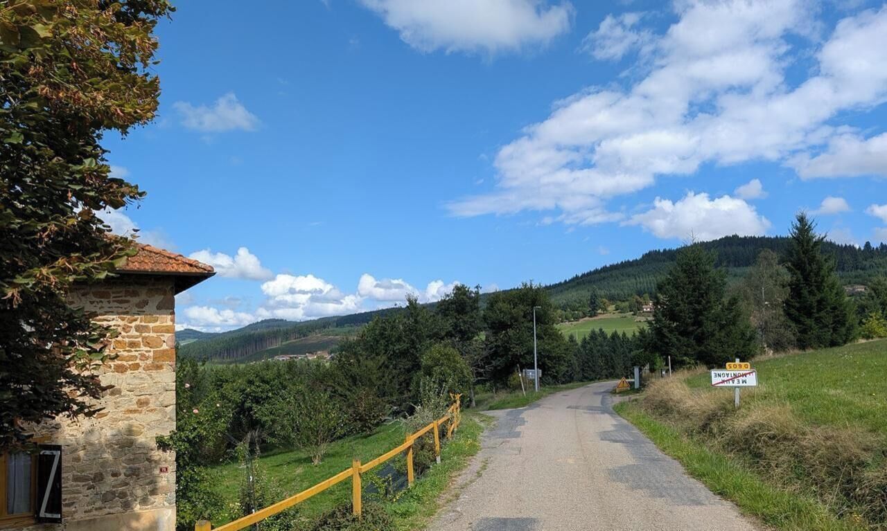 A rural road with a stone building on the left, a yellow railing, and a sign indicating a 3 km distance to a destination.