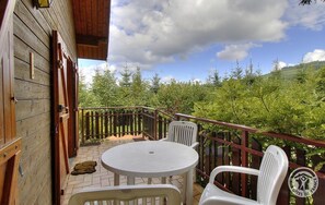 A wooden deck with a table and chairs, surrounded by a wooden railing, overlooking a forested hillside. - L'écho du temps - MEAUX LA MONTAGNE (MEAUX LA MONTAGNE)