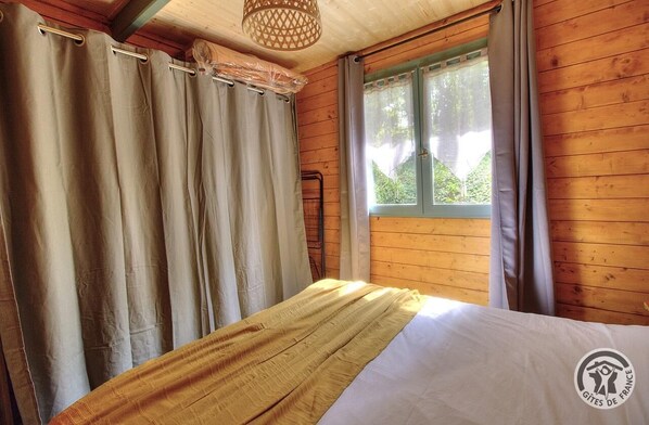Une pièce en bois avec un lit, des rideaux et une fenêtre.