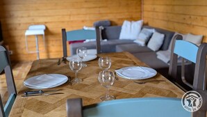 Une table à manger dressée avec des assiettes, des couverts et des verres à vin, avec un canapé et des fauteuils en arrière-plan.