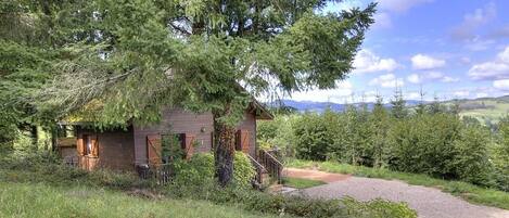 A rustic cabin with a gravel driveway and a wooden staircase leading up to the entrance.