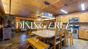 Un'accogliente sala da pranzo in stile rustico, con un grande tavolo in legno e panche, pavimento in pietra e mobili in legno.
