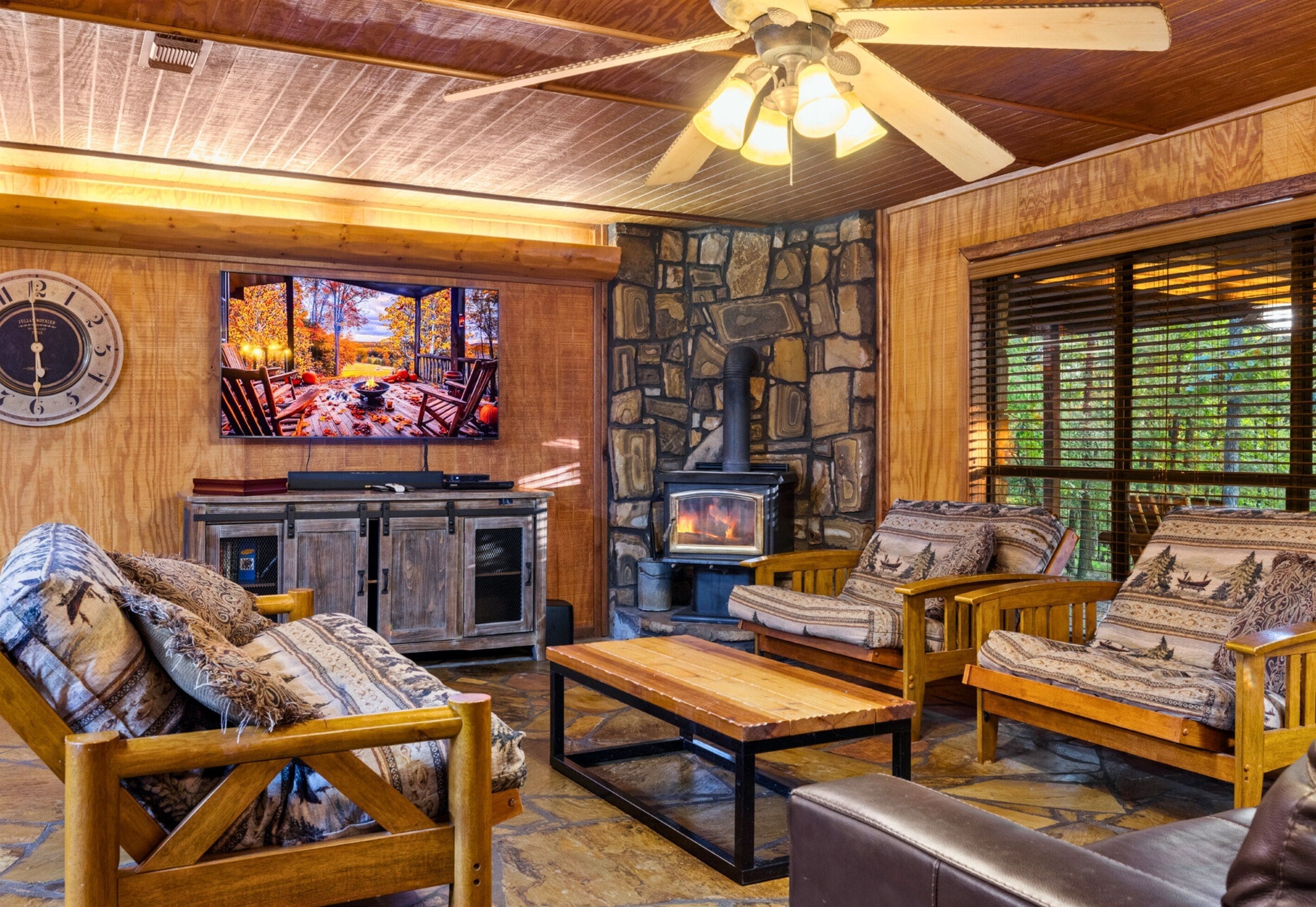 A cozy living room with a stone fireplace, wooden furniture, a television, and a clock.