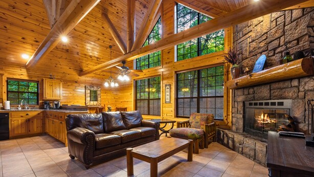 A spacious living area with a fireplace, wooden ceiling, and large windows. - Shaui Chukka Cabin | Cozy Pondside Cabin (Broken Bow)