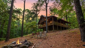 A cabin with a deck, surrounded by trees and a fire pit. - Shaui Chukka Cabin | Cozy Pondside Cabin (Broken Bow)