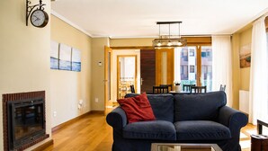 A living room with a fireplace, a sofa, a coffee table, and a dining area in the background. - Villa Playa de Barro with garden - Llanes (Llanes)